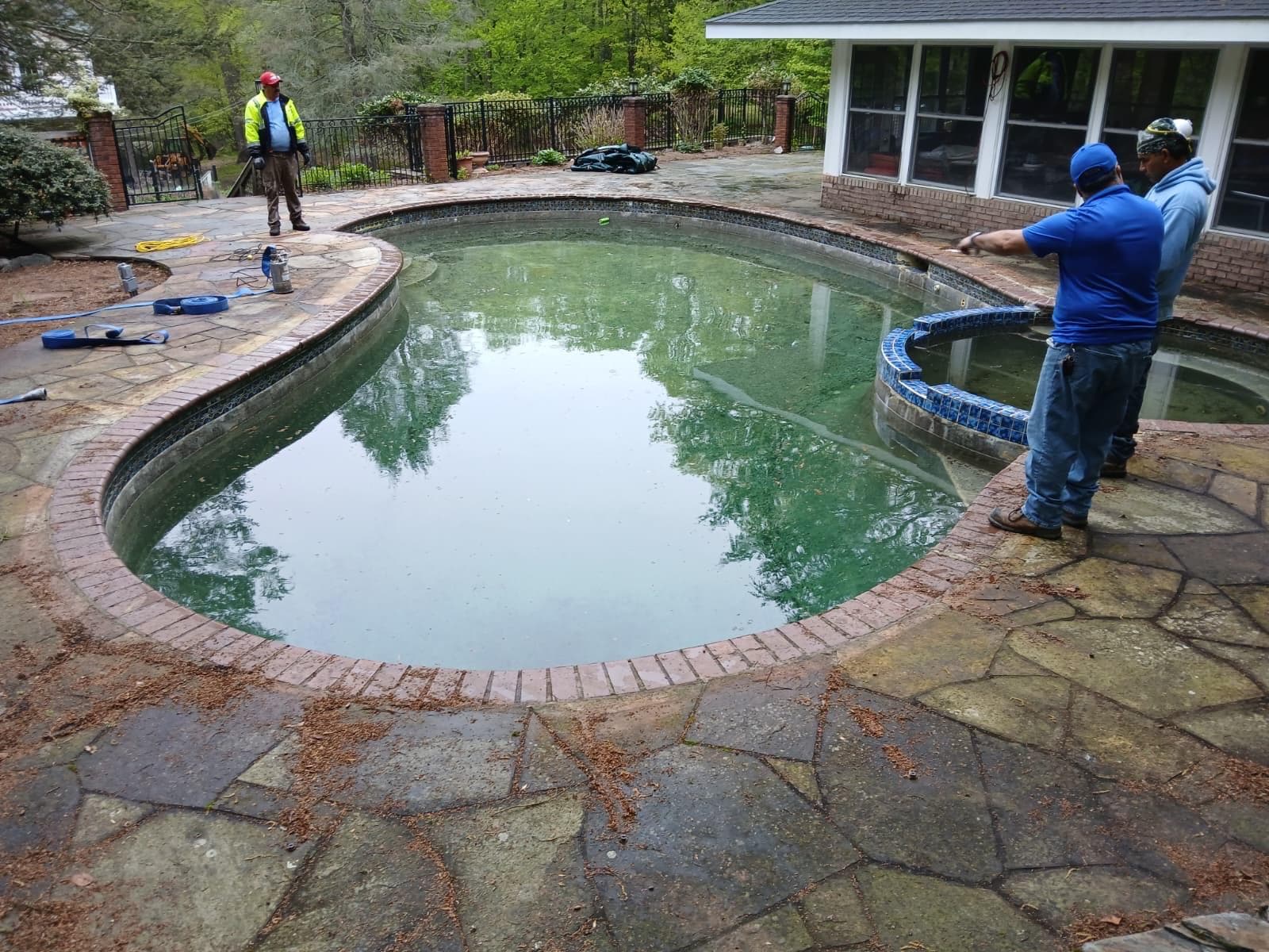 Crew servicing a green, algae-filled kidney pool with attached spa before cleaning