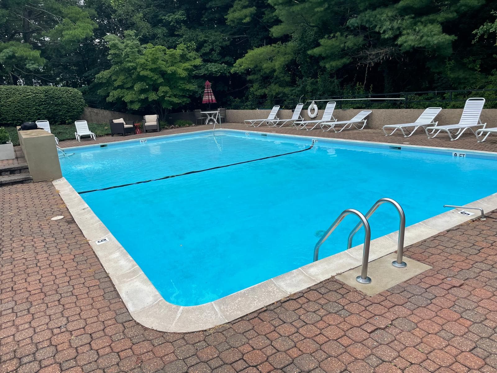 Pool with a green safety cover, paver deck, low stone wall, and wood privacy fence