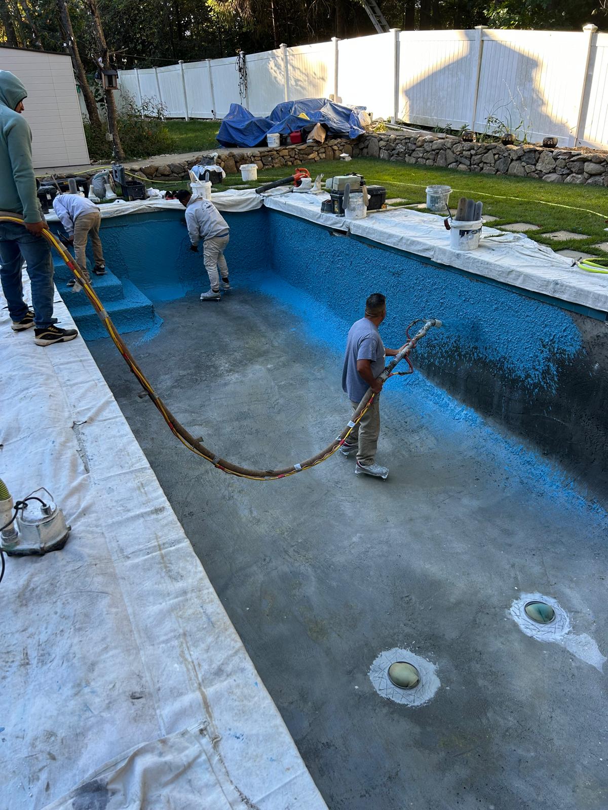 Crew applying fresh blue plaster to a drained pool shell during renovation