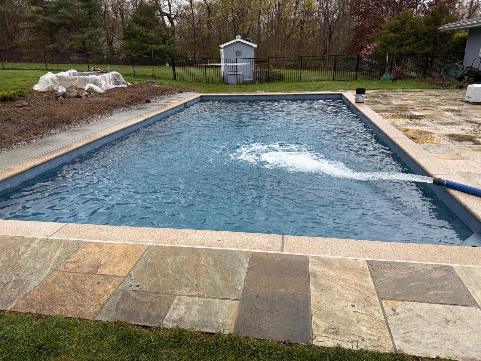 Finished rectangular pool being filled with water alongside a bluestone patio